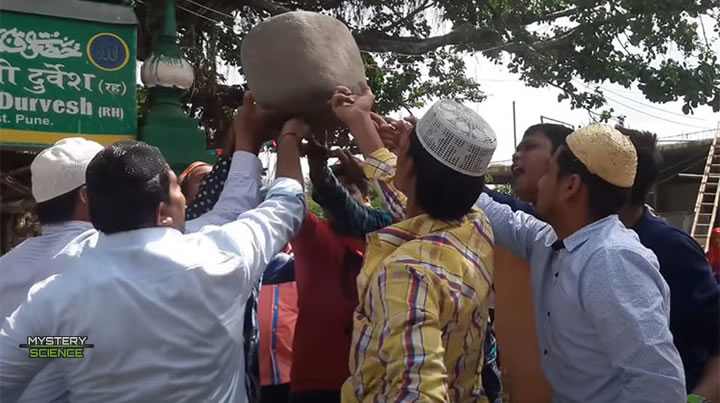 Grupo de 11 hombres levantando una roca de varios kilogramos solo con su dedo índice.